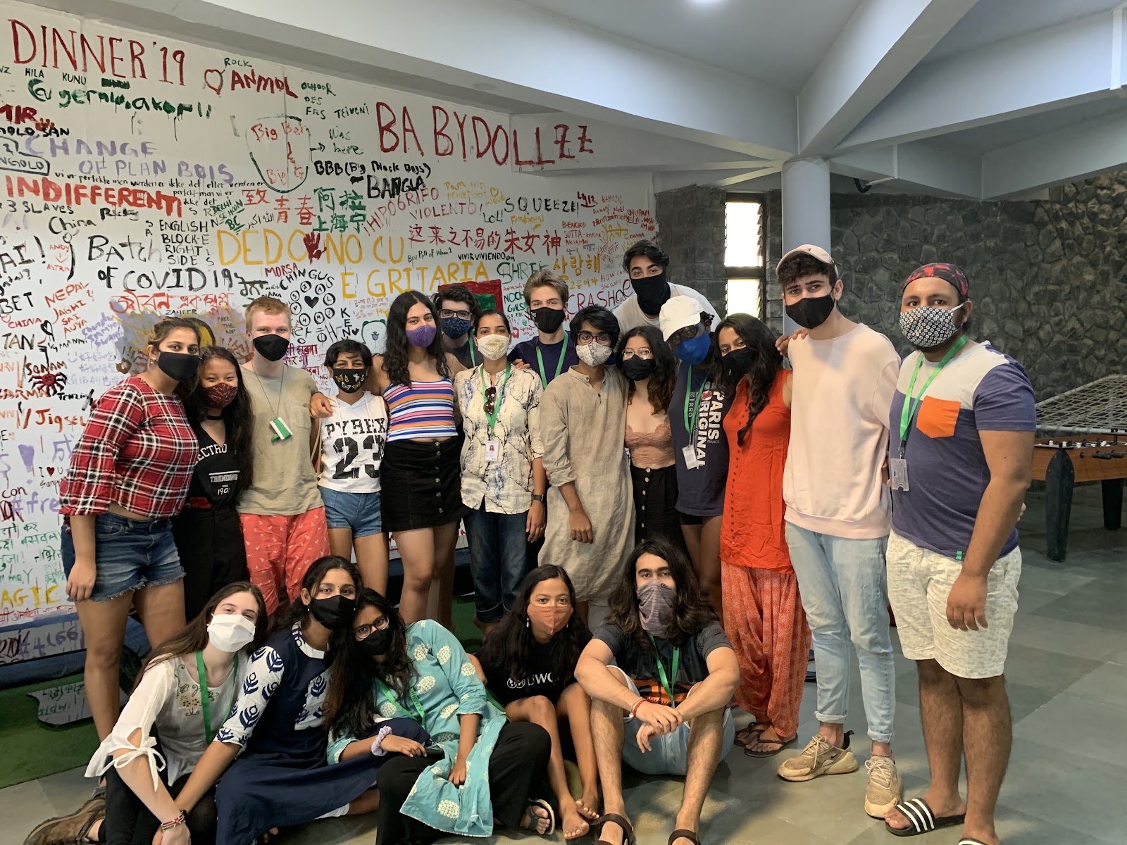 The cohort in front of a wall covered in student signatures and messages in many languages