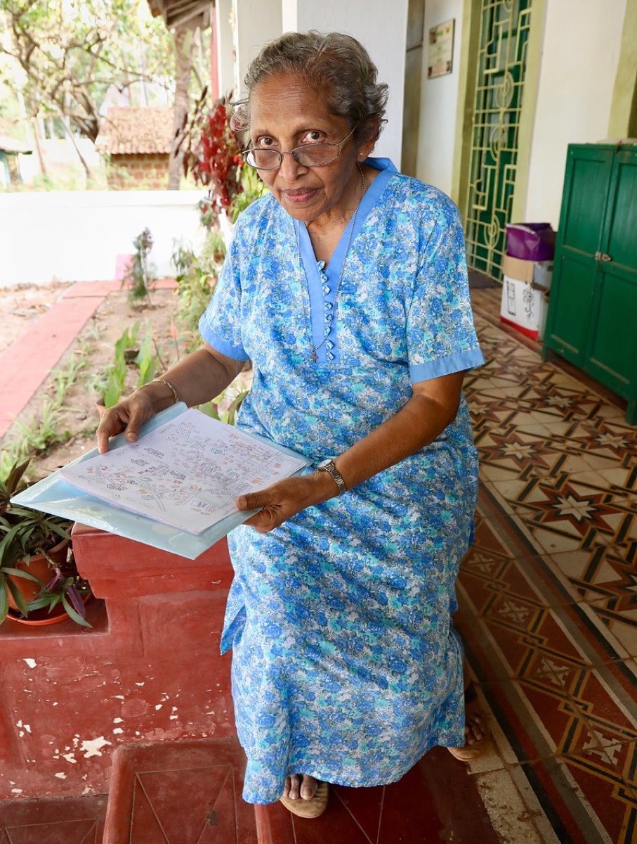 An older woman seated on a veranda, holding a hand-drawn power map made with a student